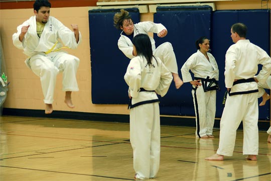 Two color belt students practice their jumping kicks while black belts stand as targets during an All-School workout.