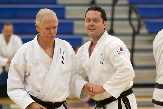 Two black belt men shaking hands and smiling.