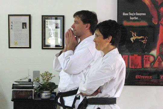 A man and women in uniform watch with a martial arts movie poster (Equal Impact) in the background.