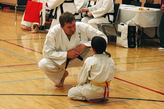 Adult referee talks to a kneeling child tournament competitor.