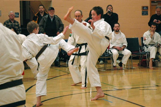 Two brown belt boys spar at a tournament. Both are in the middle of a kick.