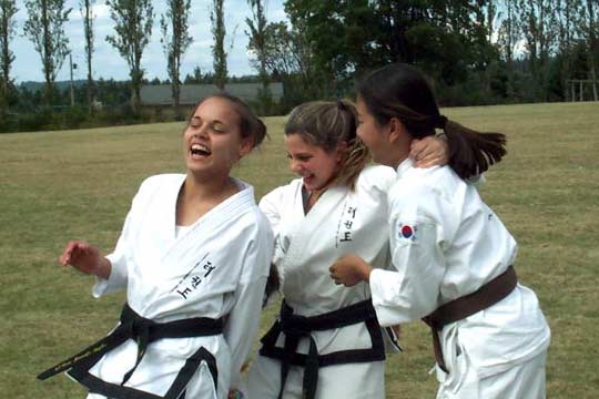 Three women in uniforms are laughing outdoors.