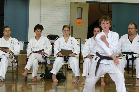 A young man does a hyung during a tournament while judges look on.