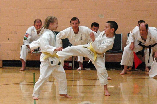 A yellow belt boy and girl spar at a tournament. 