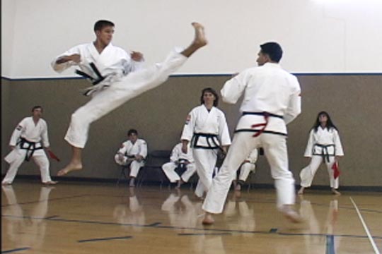 A man does a jumping kick during a tournament sparring match.