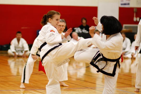 Two black belt women spar at a tournament.