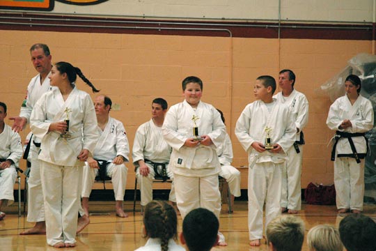 Young white belts hold their trophies during a tournament.