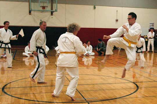 Two yellow belt men spar at a tournament. One is in the air.